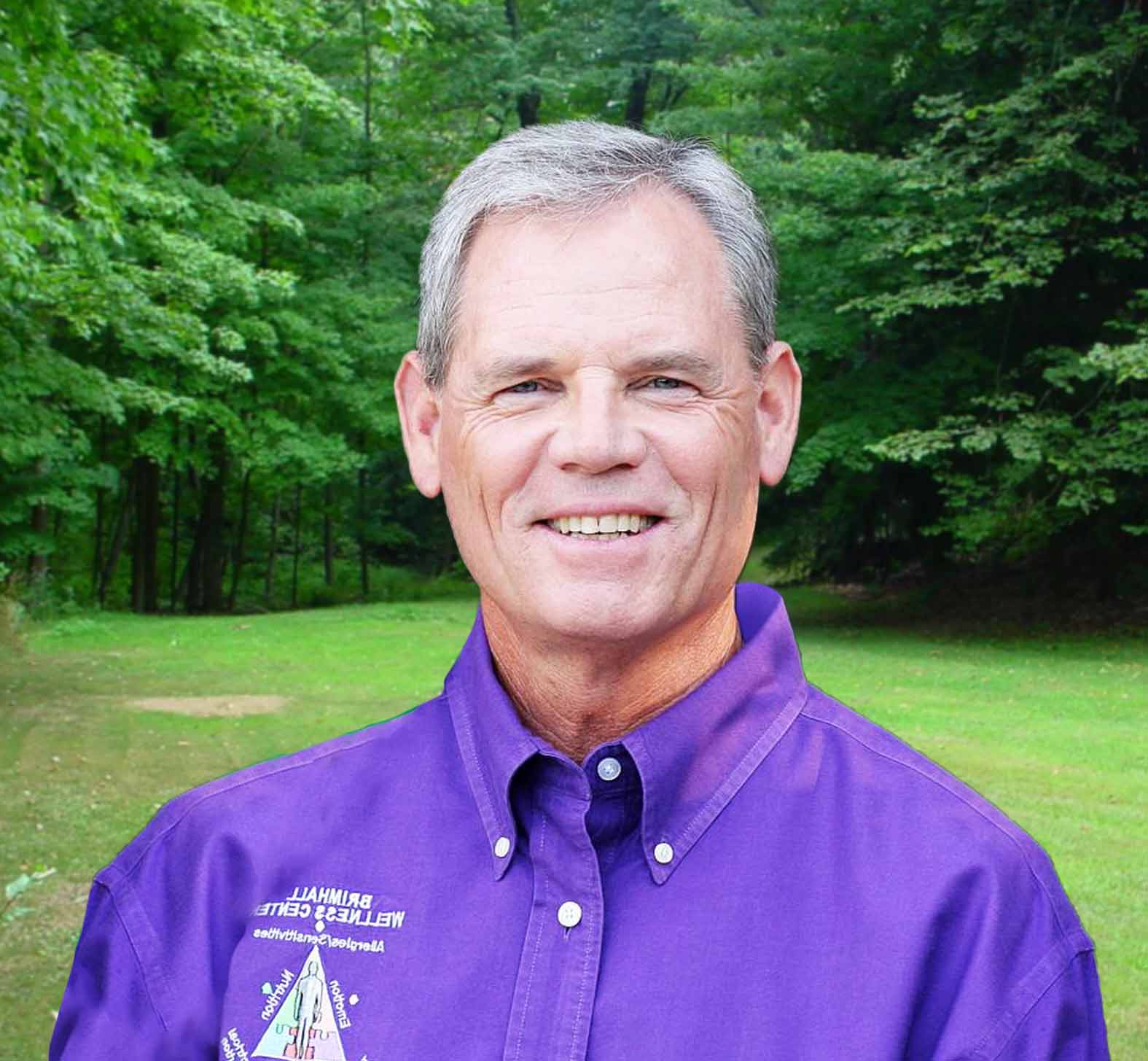 A picture of Dr. John Brimhall in a Purple shirt with a forest in the background.