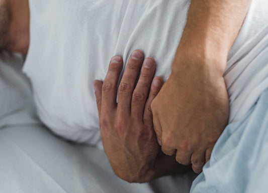 A zoomed-in picture of a pair of hands holding their stomach in pain while laying down Digestive & Gut Issues