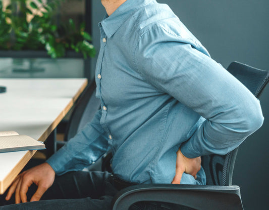 man holds his back in pain while sitting at his desk with a notebook. Fibromyalgia