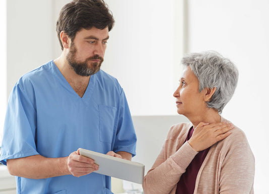 A male nurse showing an elderly lader her results on a tablet as she holds her shoulder. Osteoporosis