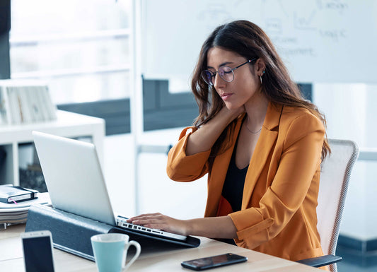 Picture of a woman working on a laptop with her left hand and her right hand holding her neck in pain and discomfort. Neck Pain & Headaches