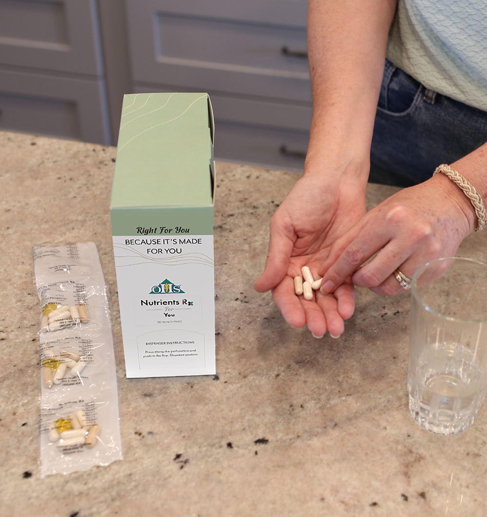 A person holding 4 supplements in their hand next to a glass of water, their custom health pak, and 4 packets of supplements.